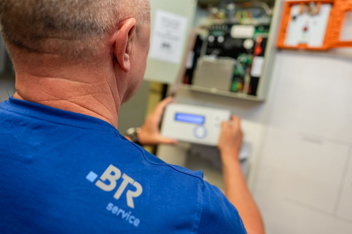 Ein Techniker in einem blauen BTR-Servicetrikot überprüft ein elektronisches Steuergerät in einem offenen Schaltschrank.