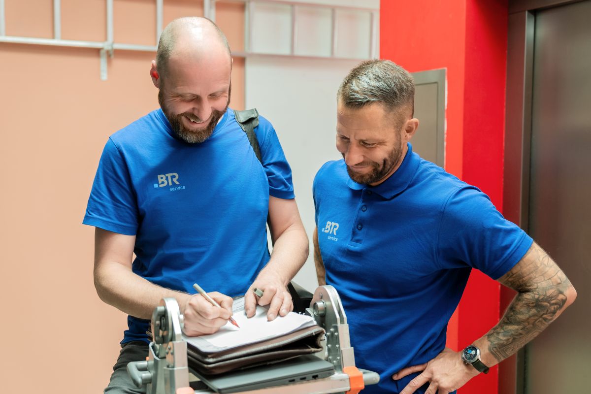 Zwei Handwerker in blauen BTR-Servicetrikots arbeiten lächelnd an einem Auftrag.